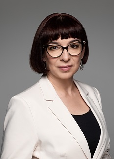 Kobieta, szatynka z krótkimi włosami do ramion, w okularach, białej marynarce i czarnej bluzce. Jest to członkini Zarządu Katarzyna Dubaniewicz